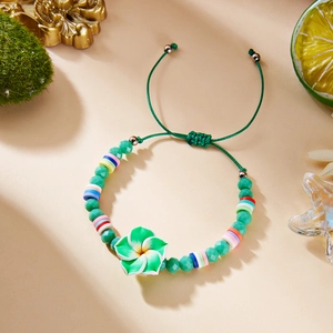 Detail of handmade braided bracelet with colorful clay beads and a green flower charm