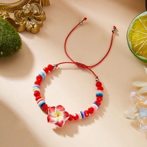 Detail of handmade plumeria flower charm bracelet with colorful clay beads and red cord