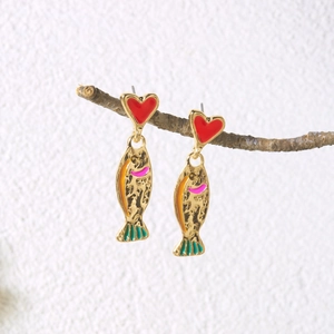Artistic close-up of fish earrings with red heart studs hanging on a natural branch