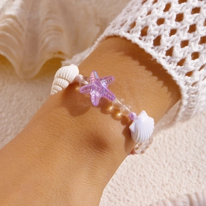 Detail eines Strandarmbands mit lila Seestern, Muscheln und Perlen am Handgelenk
