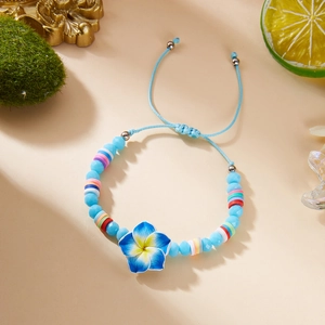 Detail of blue plumeria flower pendant and colorful clay beads on handwoven bracelet