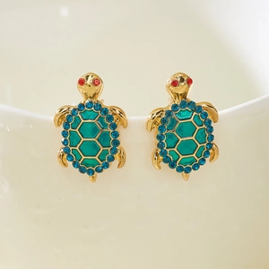 Detail of gold-plated turtle earrings with green enamel and blue crystals on white porcelain