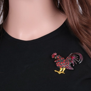 Détail d'une broche coq colorée avec strass rouges portée sur un vêtement noir élégant