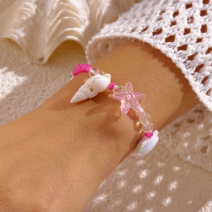 Detail eines rosa Strandarmbands mit Seestern-Anhängern und Muschelperlen im Sand