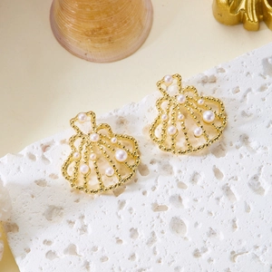 Detailed view of golden shell earrings with white pearls on a textured stone