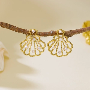 Detailed view of scallop-shaped gold metal earrings featuring small white pearls and openwork