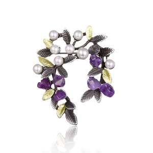 Macro view of a vintage wreath brooch featuring pearls, purple crystals, and silver leaves