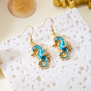 Macro detail of blue enamel seahorse earrings with crystal accents on white coral