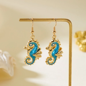 Detail view of gold seahorse earrings with blue enamel and rhinestones on a gold stand