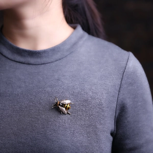 Detailansicht einer Bienenbrosche aus Legierung mit weißen Emailleflügeln auf grauem Pullover