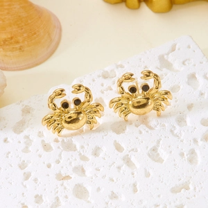 Detail shot of gold crab stud earrings with black gem eyes on white stone texture