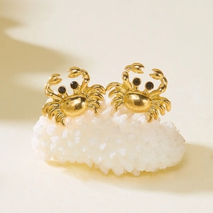 Detailed close-up of golden crab stud earrings with black stone eyes on white coral reef