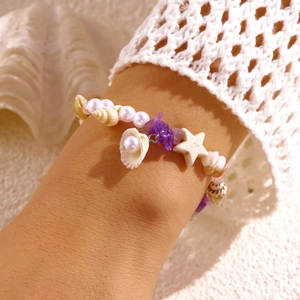 Detailansicht Strandarmband mit Muscheln, Seestern und lila Steinen am Handgelenk