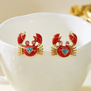 Detail of red enamel crab earrings with blue crystals and mini pearl on white ceramic