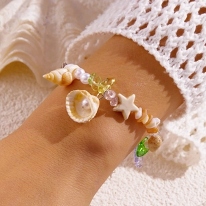 Detail eines Strand-Perlenarmbands mit natürlichen Muscheln und Seestern am Handgelenk