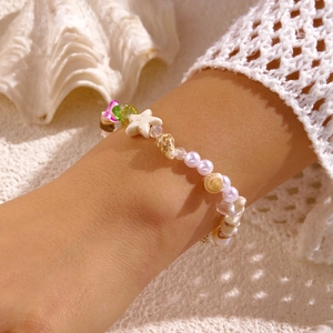 Detailaufnahme von Perlenarmband mit Seestern und Muscheln auf Sandhintergrund