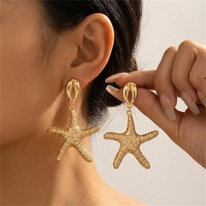 Detalle de pendientes de estrella de mar dorados con pernos de concha en modelo