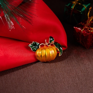 Close-up of a pumpkin brooch with orange enamel and green leaves on a festive background
