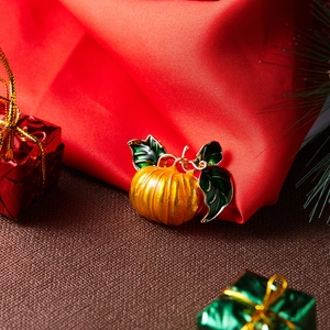 Macro detail of pumpkin brooch with orange enamel and green leaves on red silk