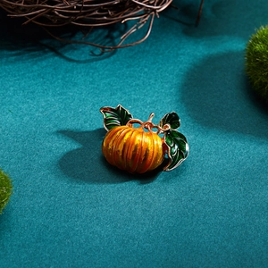 Detailed view of orange enamel pumpkin brooch with gold metal base and green leaves