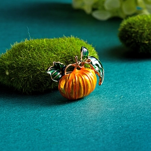 Detailed close-up of an orange enamel pumpkin brooch with green leaves on moss