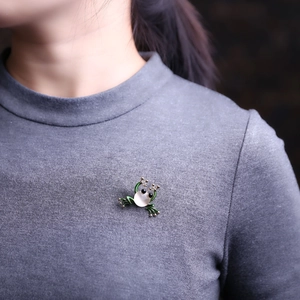 Schicke grüne Froschbrosche mit Opal-Bauch auf grauem Strickstoff einer Jacke