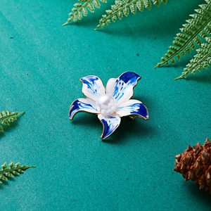 Elegante blaue Blumenbrosche mit Perle, Goldkanten und Emaille-Finish vor Naturhintergrund