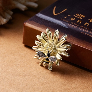Close-up of golden daisy brooch with rhinestone bee and enamel texture detail