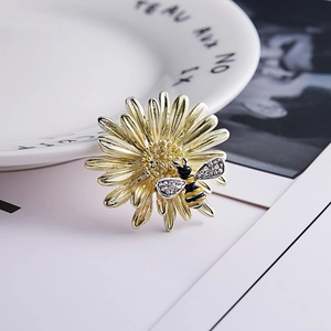 Elegant gold daisy flower brooch with rhinestone bee detail on artistic background