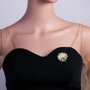 Detailed view of a golden daisy brooch with a small bee on a black dress lapel