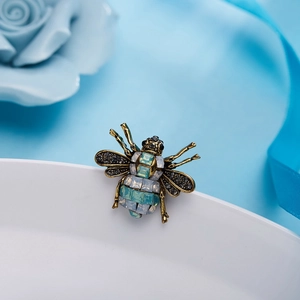 Macro detail of vintage gold bee brooch with light blue crystals on a white plate