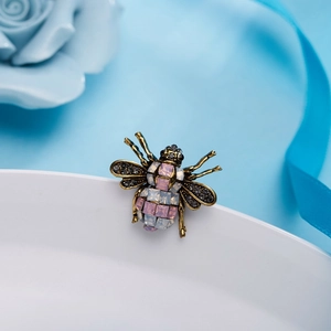 Vintage gold bee brooch with pink and white crystals on a white ceramic plate