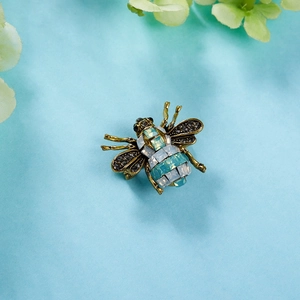 Vintage gold bee brooch with black and green crystals on light blue background