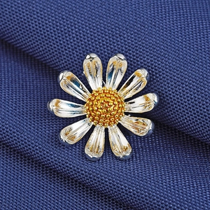 Élégante broche marguerite avec pétales argentés et cœur doré sur tissu bleu foncé