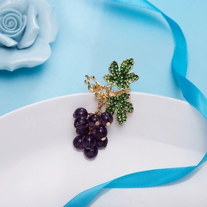 Détail macro de la broche raisin avec perles violettes et feuilles en strass verts