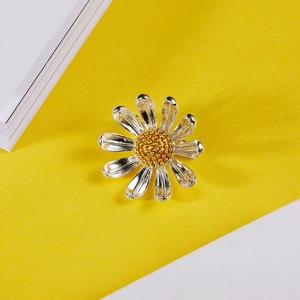 Détail d'une broche marguerite argentée avec pistil doré sur fond jaune et blanc