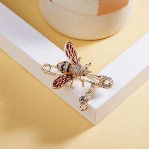 Détail macro d'une broche abeille avec ailes en cristal, émail rouge et pendentif alvéole