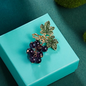 Broche raisin violette étincelante avec feuilles en cristal sur boîte à bijoux bleue