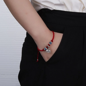 Close-up of red braided rope bracelet featuring evil eye beads and silver elephant charm