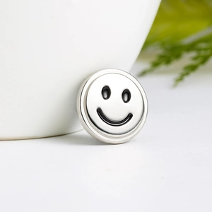 Minimalist silver airplane brooch with black enamel smiley face on a white ceramic cup