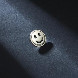 Macro detail of a polished silver metal smiley face pin with sharp shadow on textured grey