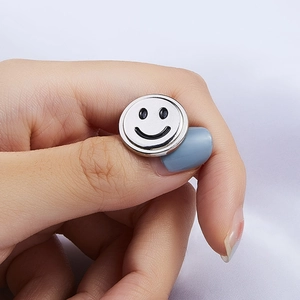 Macro shot of a silver metal smiley face badge held by hand on soft silk fabric