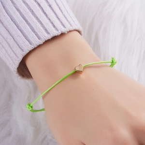 Verstellbares neongrünes Kordelarmband mit goldenem Herzanhänger auf weißem Kunstfell