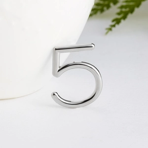 Detailed view of silver number five shaped ear cuff on minimalist white ceramic background