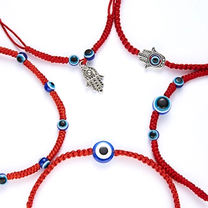 Macro shot of handmade red rope bracelets featuring blue evil eye beads and hamsa hand charms