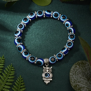 Blue Evil Eye bead bracelet with silver owl charm on a deep green textured background