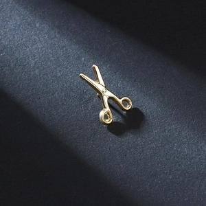 Macro shot of minimalist gold scissors brooch with polished finish on black surface