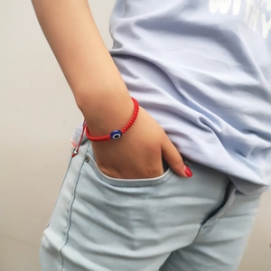 Detail of red braided evil eye bracelet worn on wrist with adjustable cord and blue bead