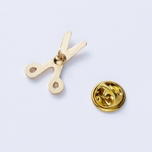 Macro view of gold scissor brooch with a butterfly clutch pin backing on white surface