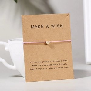 Rosa Kordelarmband mit goldenem Herzanhänger auf Kraftpapier-Karte als Geschenk